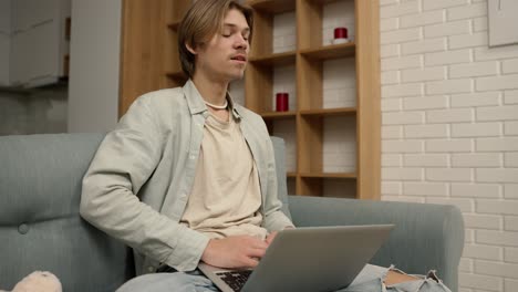 Un-Joven-Sentado-En-Un-Sofá-Trabajando-Desde-Casa-Con-Una-Computadora-Portátil