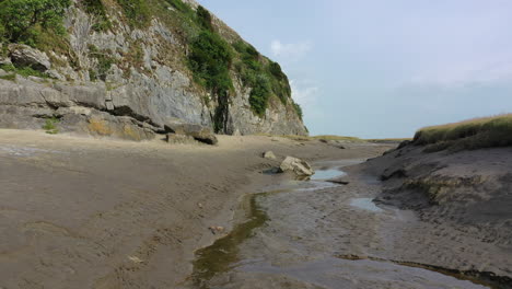 low moving shot along the sand at the bottom of a cliff, at low tide on a bright day