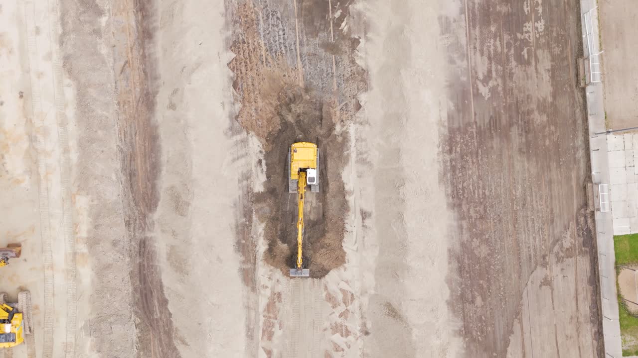 Vertical aerial view showing an excavator in action as it digs and levels soil for a football field renovation project