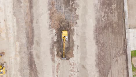 vertical aerial view showing an excavator in action as it digs and levels soil for a football field renovation project