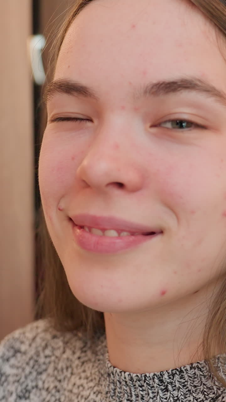 Teen girl smiling, Happy teenager with natural skin features, Young woman relaxes in warm indoor lighting with freckles, Close view of cheerful girl showing authentic skin and cozy atmosphere