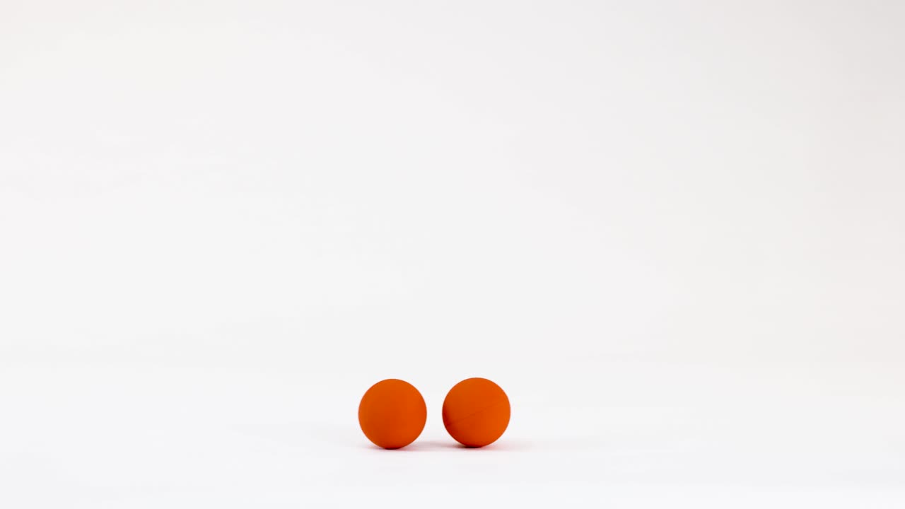 Two orange balls roll and bounce across a clean white surface with minimalist studio lighting