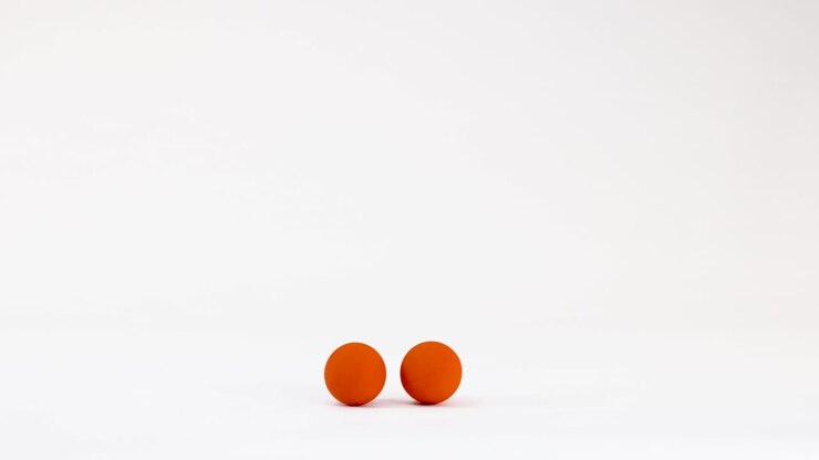 Two orange balls roll and bounce across a clean white surface with minimalist studio lighting