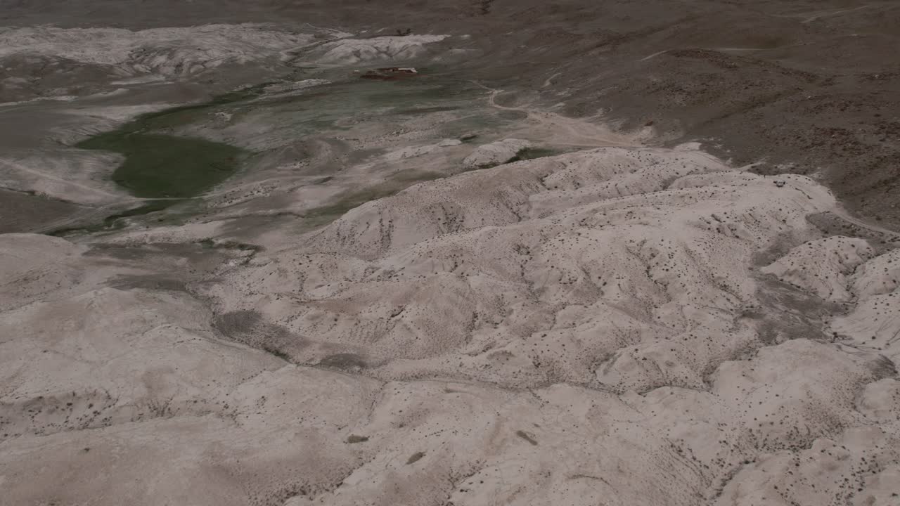 Drone footage of barren Altai landscape with eroded hills and a winding dry riverbed, with a small green water pool in the valley, Altai Republic, Russia