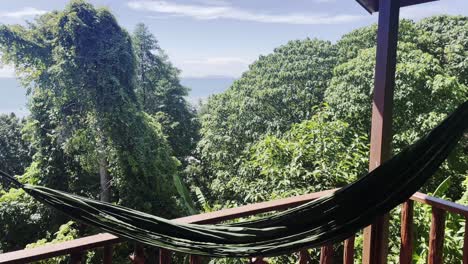 green hammock hanging in a wooden view point above the trees, sunny day with epic view in the forest of an island, static shot