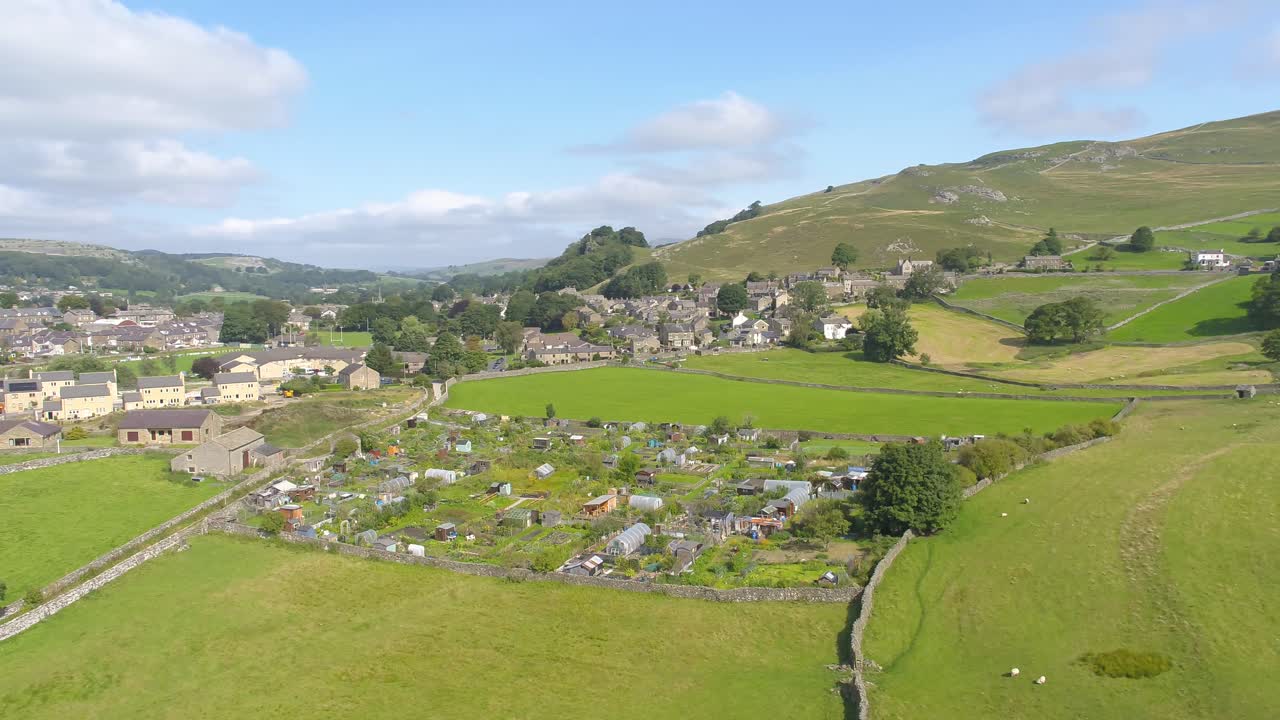 imágenes de drones moviéndose lateralmente, panorámicas y ascendentes revelando las colinas y el campo alrededor del pueblo de settle, yorkshire, reino unido, incluidas tierras de cultivo, casas, campos, muros de piedra y asignaciones