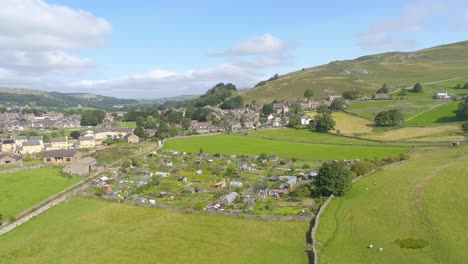 drone footage moving sideways, panning and ascending revealing the hills and countryside around the village of settle, yorkshire, uk, including farmland, houses, fields, stone walls and allotments