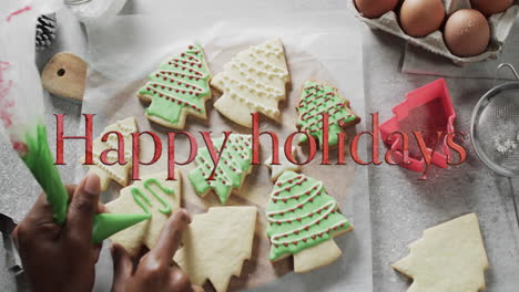 Happy-holidays-text-in-red-over-decorated-christmas-cookies-on-kitchen-worktop