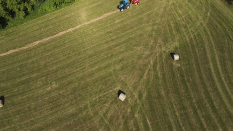 Aerial-View-Of-Tractor-With-Round-Baler-Over-Wheat-Fields-During-Harvest-Season