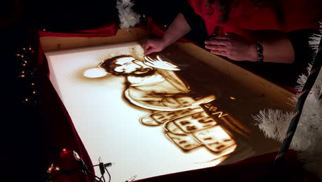 woman painting beautiful picture with sand on illuminated glass screen