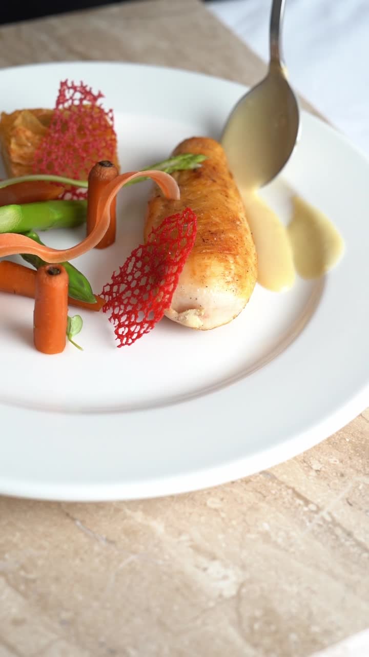 Chief puts sauce on roasted chicken piece with carrots and green beans on a plate, close up shot, insert shot