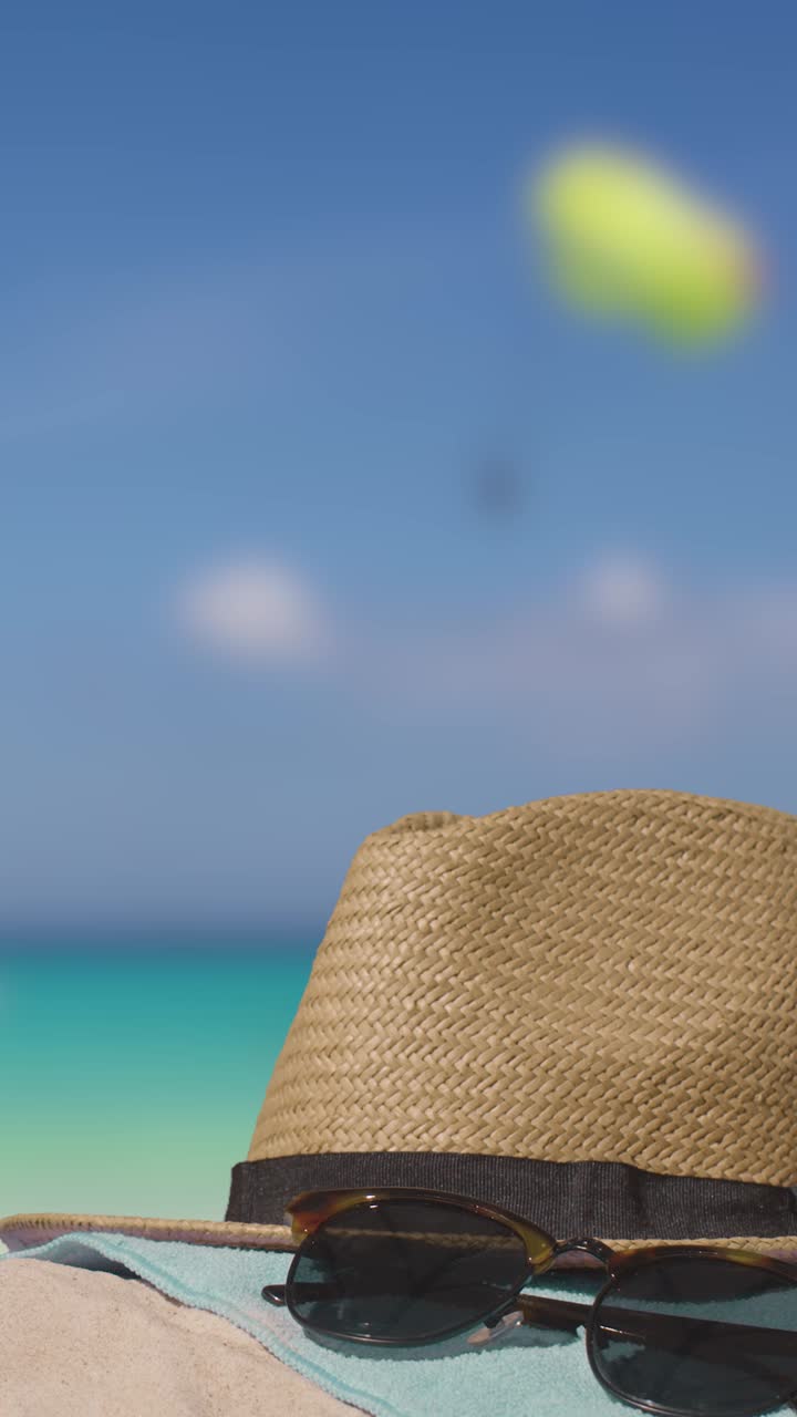 video vacanza estiva verticale concetto di occhiali da sole cappello da spiaggia asciugamano sulla sabbia contro il mare con parapendio