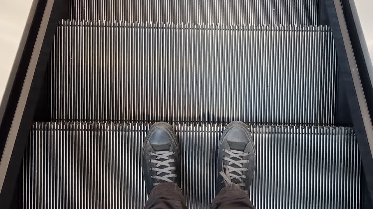 pies masculinos en zapatillas negras en escaleras mecánicas en centro comercial, vista superior pov