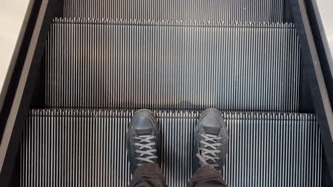 male feet in black sneakers on escalator in shopping mall, top view pov