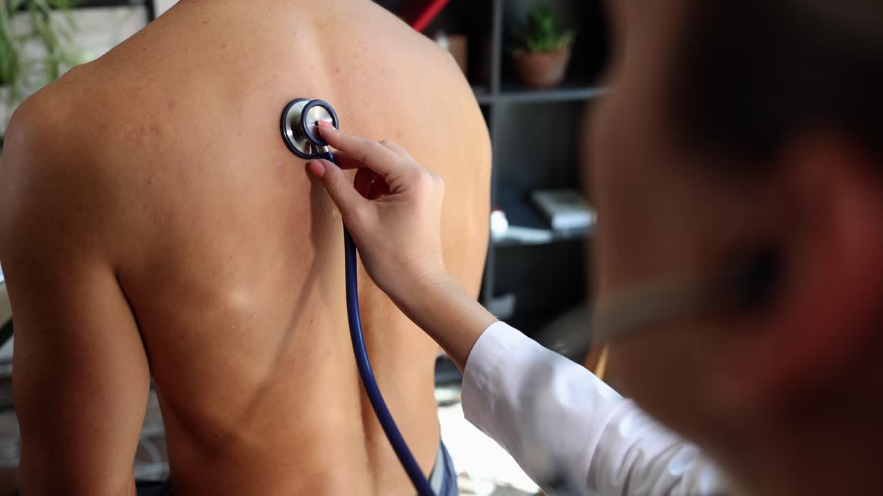Doctor uses stethoscope to examine patient's back during a medical check-up