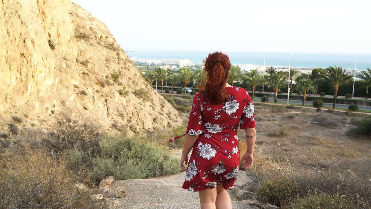 Woman in red dress walking towards a city landscape with palm trees