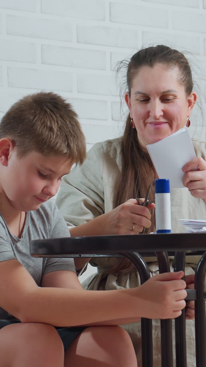 Madre e hijo caucásicos haciendo manualidades en una mesa, usando papel y pegamento, interior acogedor de ladrillo blanco, la madre guía al niño a través del corte y pegado, caras sonrientes, manos trabajando, momento familiar de cariño
