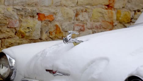 close-up of the headlights, chrome radiator grille and small statuette of a deer on the body of a snowy russian volga m21