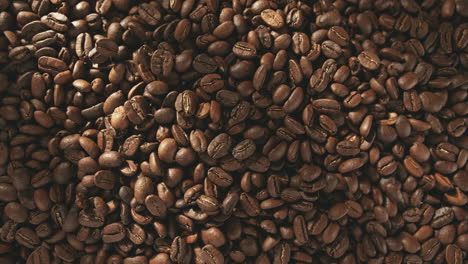 handful of coffee beans falling onto a pile of freshly roasted grains - top view