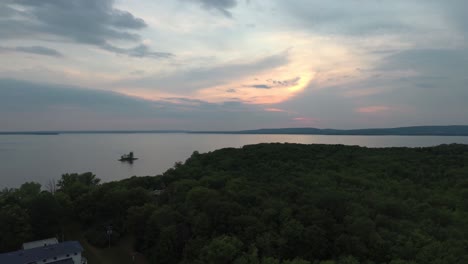 Drone-flying-over-forest-at-dawn-at-towards-lake-and-pink-skies