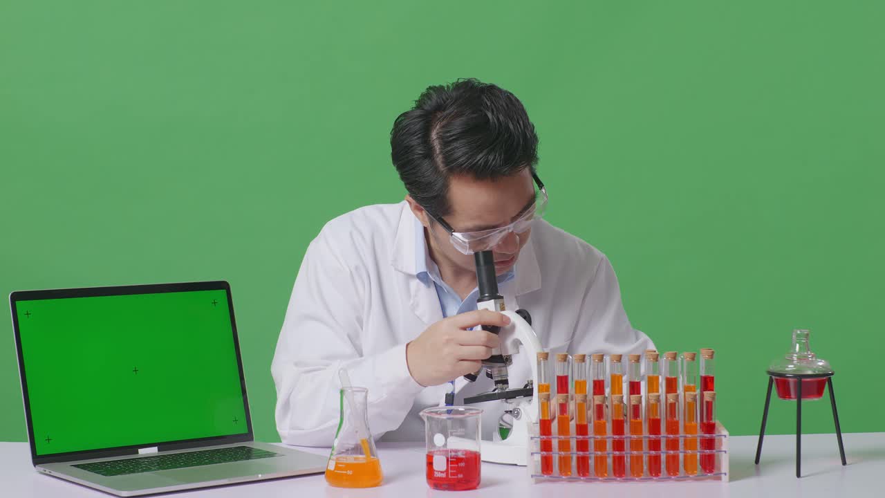 Asian Man Scientist Working On The Table With Microscope And Test Tube And Green Screen Laptop In The Green Screen Background Laboratory