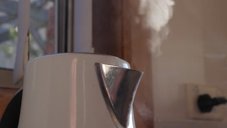 pan up of boiling water and steam coming out of white modern kettle