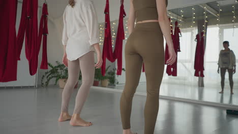 back view of inner peace seekers shaking bodies mindfully while facing mirror during yoga session, surrounded by red aerial hammocks and soft lighting in indoor studio for spiritual movement practice