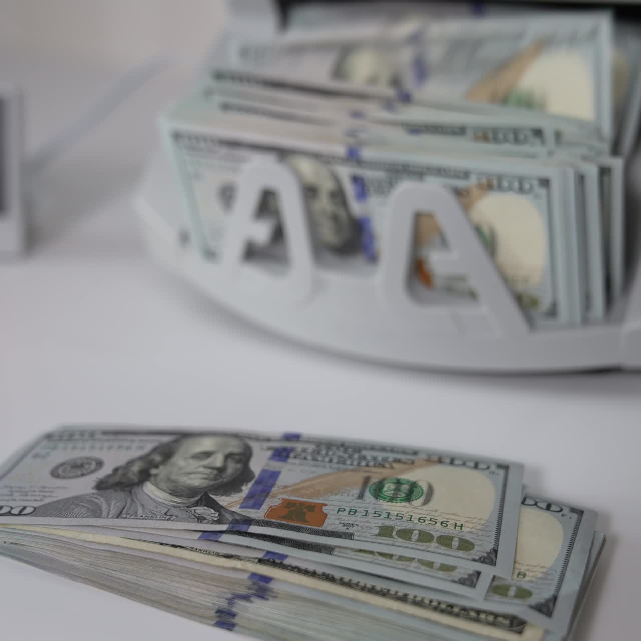 One hundred dollar banknotes on the table and in the cash counting machine. Male hand takes a wad of money showing them to the camera. Close up