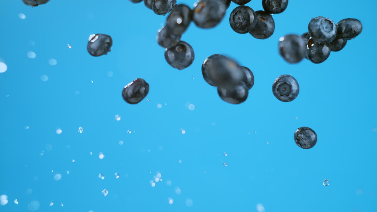 A bunch of wet blueberries flying through the frame. High quality cinematic studio commercial super slow motion 1000fps shot of fresh berries moving up and down on a blue background.
