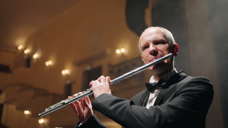 flutist is playing flute blowing air in wind instrument concert in old opera house or modern music hall