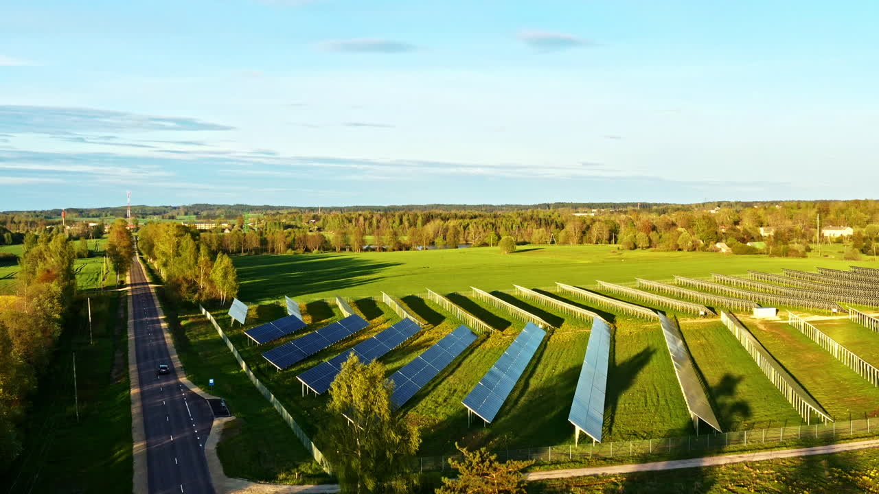 Wide Solar Panel Field Beside Country Road Surrounded by Forest in Golden Hour Sunlight at Evening