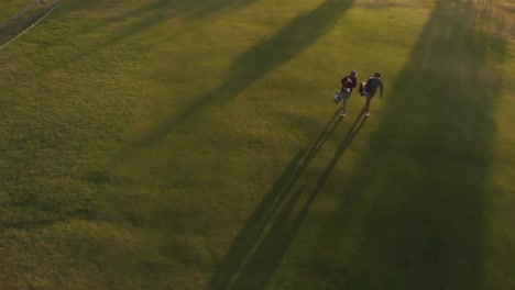 Two-diverse-male-golf-players-walking-at-golf-course-on-sunny-day