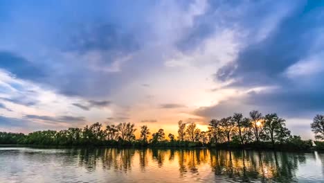 Beautiful-timelapse-footage-of-trees-a-lake-and-gorgeous-sky-in-the-background-that-has-orange,-yellow-and-blue-colors