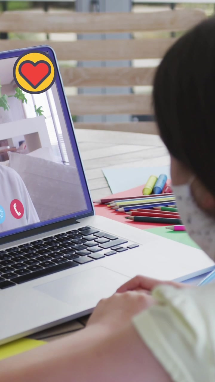 Animación de iconos de corazón sobre una chica con mascarilla usando una laptop en una videollamada