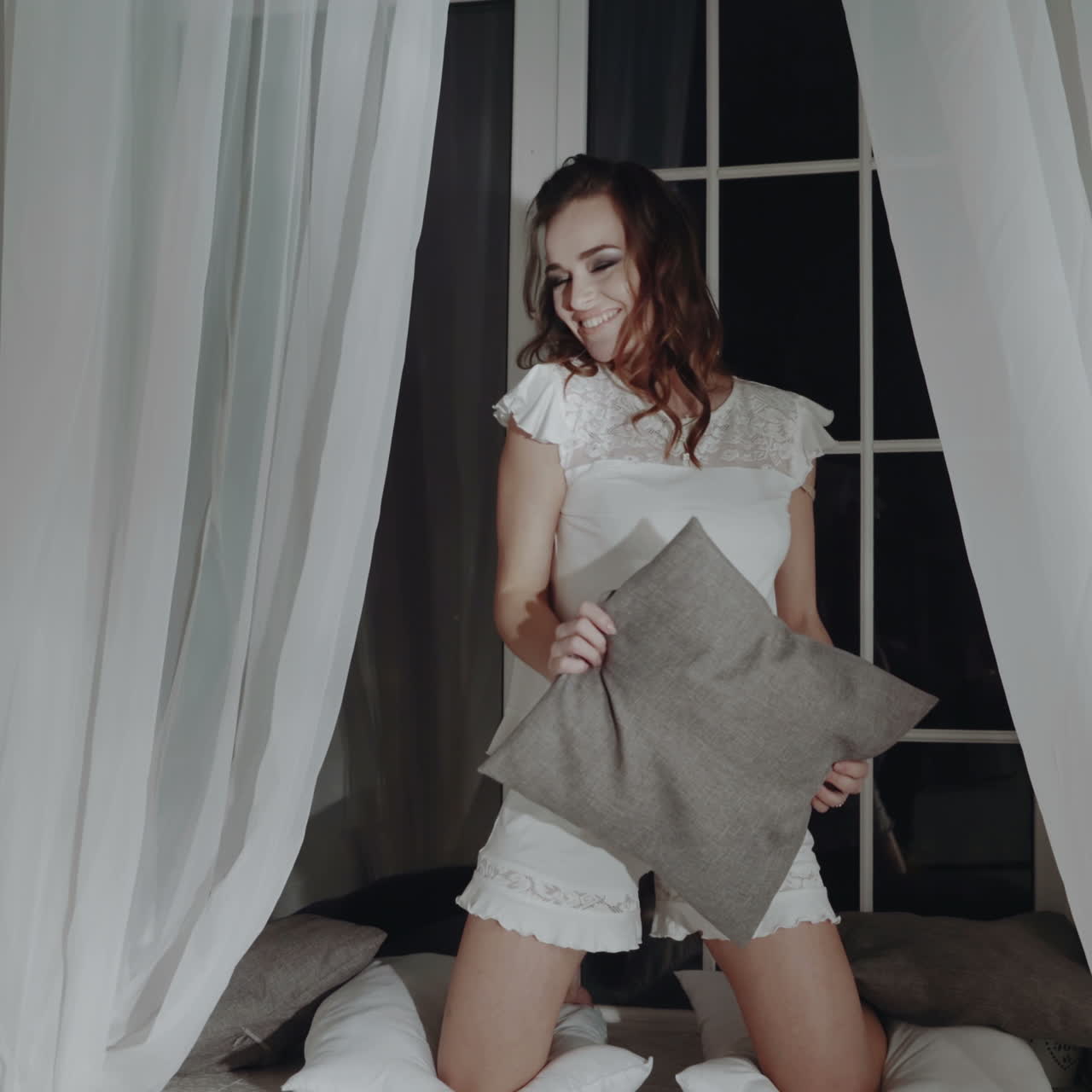 Woman having fun with a pillow in her bedroom at night