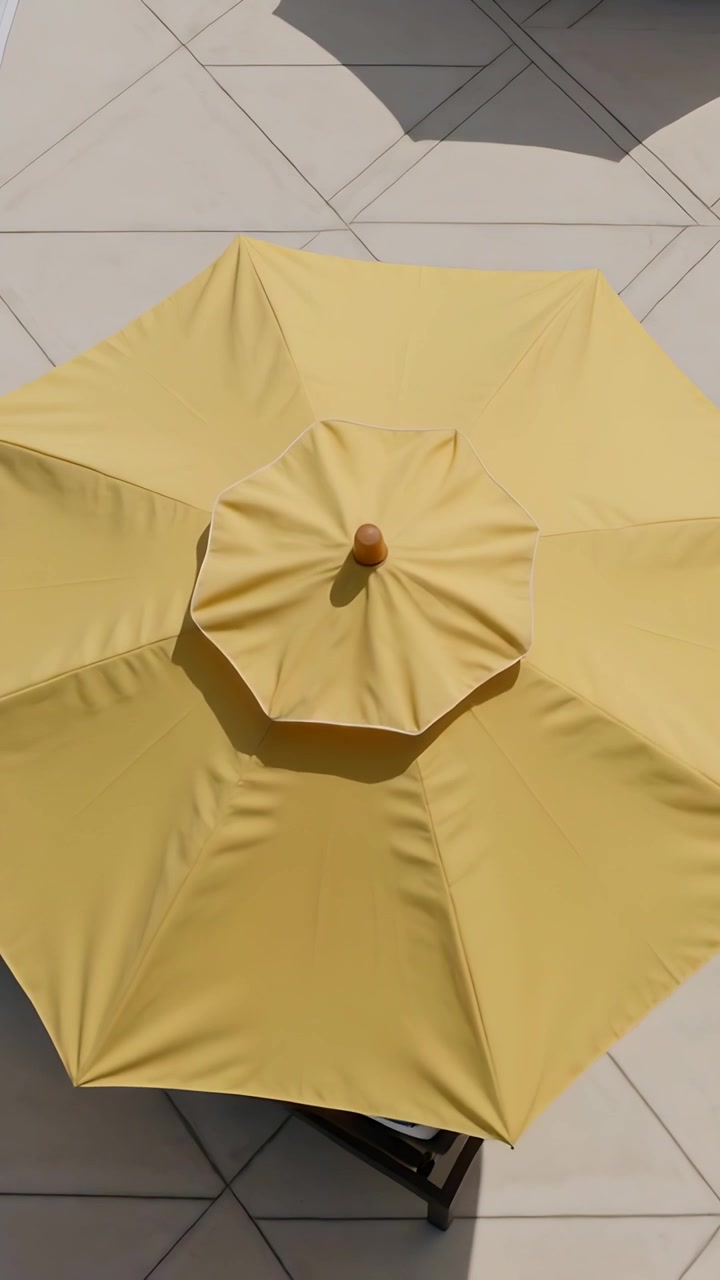 Video verticale: Ombrellone da patio giallo che si apre e si dispiega sopra il bordo piscina, rivelando un puntale in legno.