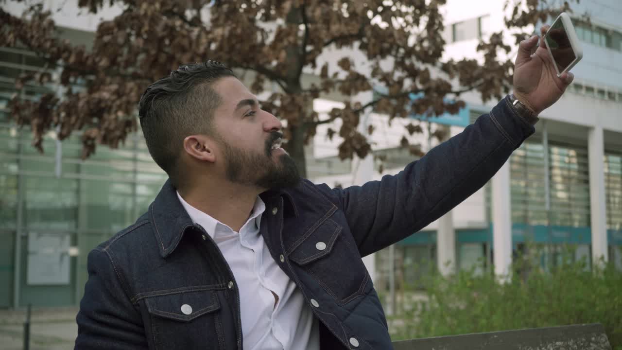 hombre barbudo feliz teniendo video chat al aire libre