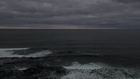 Drone-shot-flying-backwards-over-a-lighthouse-on-a-moody-dramatic-morning-or-evening-overlooking-the-ocean