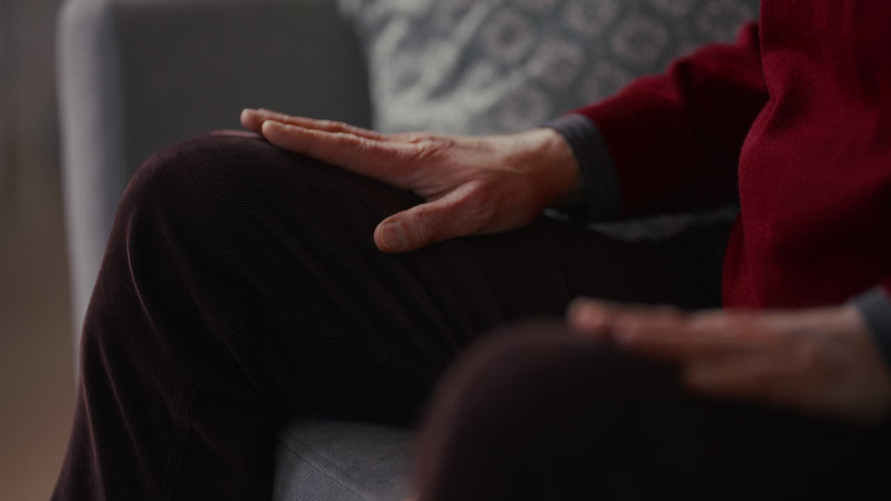 Nærbillede af mands hænder, der hviler på knæene, mens han sidder