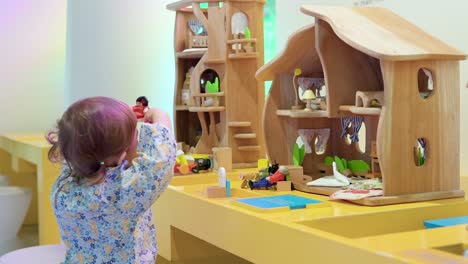 2-year-old toddler girl creatively playing with doll figures in a dollhouse