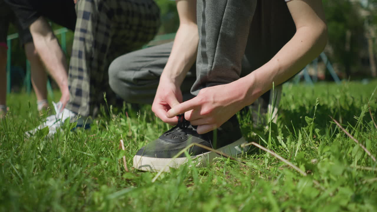Close-up of three people on a grassy field, two of them squatting to adjust their shoelaces while a young child stands nearby