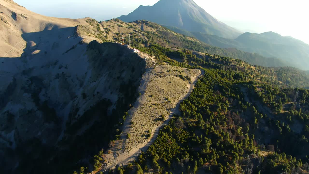Drone aerial tilt up view from dense pine forest to Arenales ridge at Nevado de Colima National Park and distant Colima Fire Volcano, Mexico