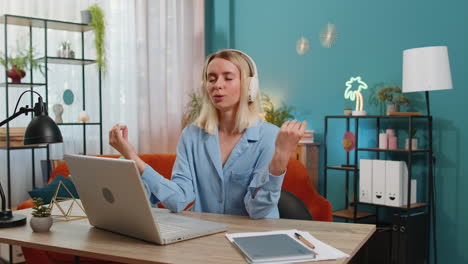 young woman in headphones meditating doing yoga breathing exercise relaxing sitting at home office