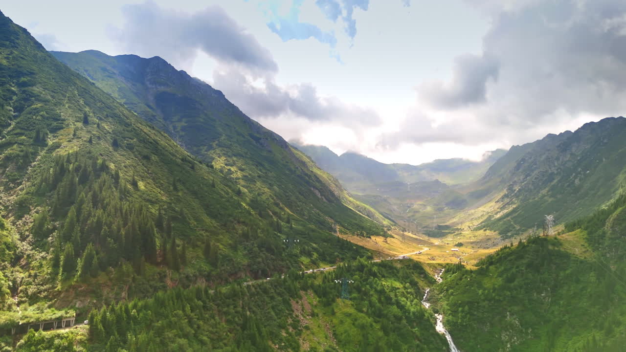 Stunning mountain valley view. Vast green mountains frame a deep valley, with a winding river and cloudy sky creating a dramatic backdrop