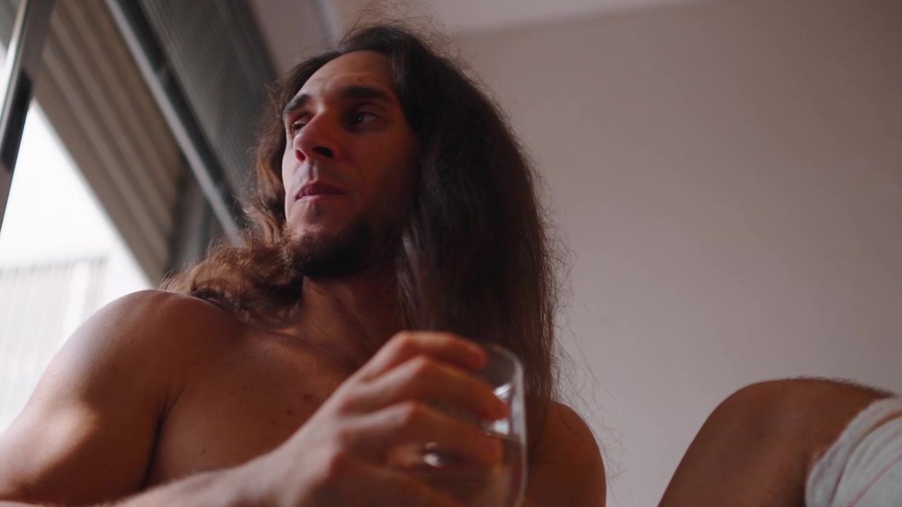 Giovane uomo con i capelli lunghi che beve acqua a casa