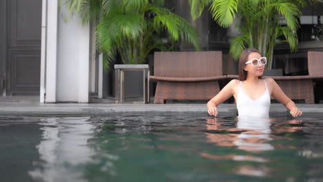 a pretty young fit woman leans back along the edge of a pool enjoying the resort lifestyle