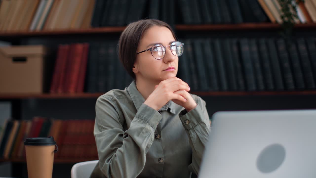 Pensive academic female working laptop at library desk thinking planning job educational project