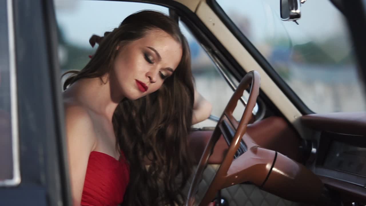 Donna in abito rosso alla guida di un'auto d'epoca