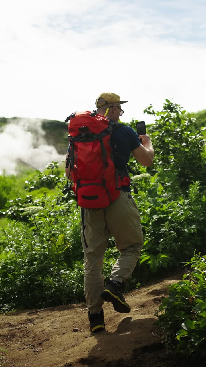 Uomo con zaino rosso che fa trekking su un sentiero di montagna verdeggiante