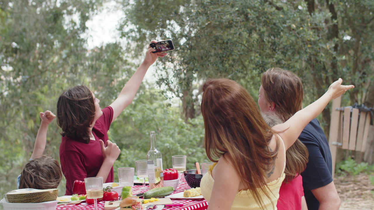 joven caucásico tomando selfie con su familia durante la cena al aire libre